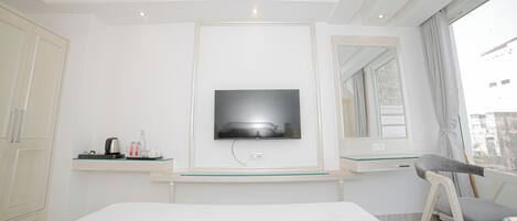 A hotel room with a bed, a TV mounted on the wall, a desk with a chair, and a window with curtains.