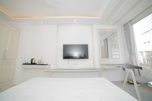 Une chambre d’hôtel avec un lit, un téléviseur fixé au mur, un bureau avec une chaise et une fenêtre avec des rideaux.