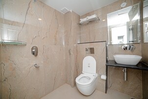 A modern bathroom with a marble floor, a white toilet, a glass shower enclosure, a sink with a mirror, and a towel rack.