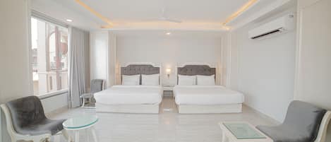Habitación de hotel con dos camas, una zona de estar con sillas y una mesita, un ventilador de techo y una ventana con cortinas.