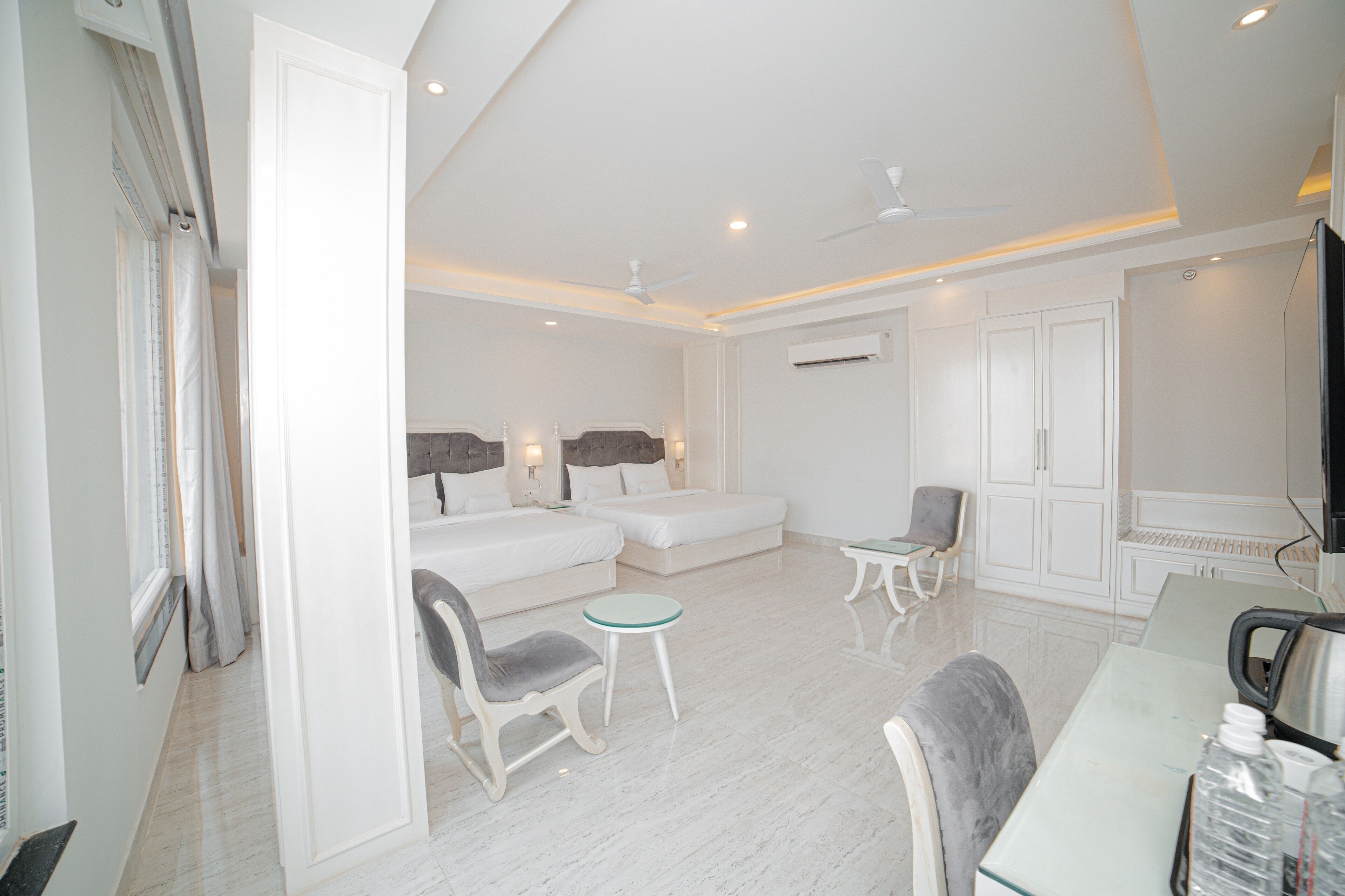 A modern hotel room with a large bed, two smaller beds, a sitting area with a table and chairs, and a television.