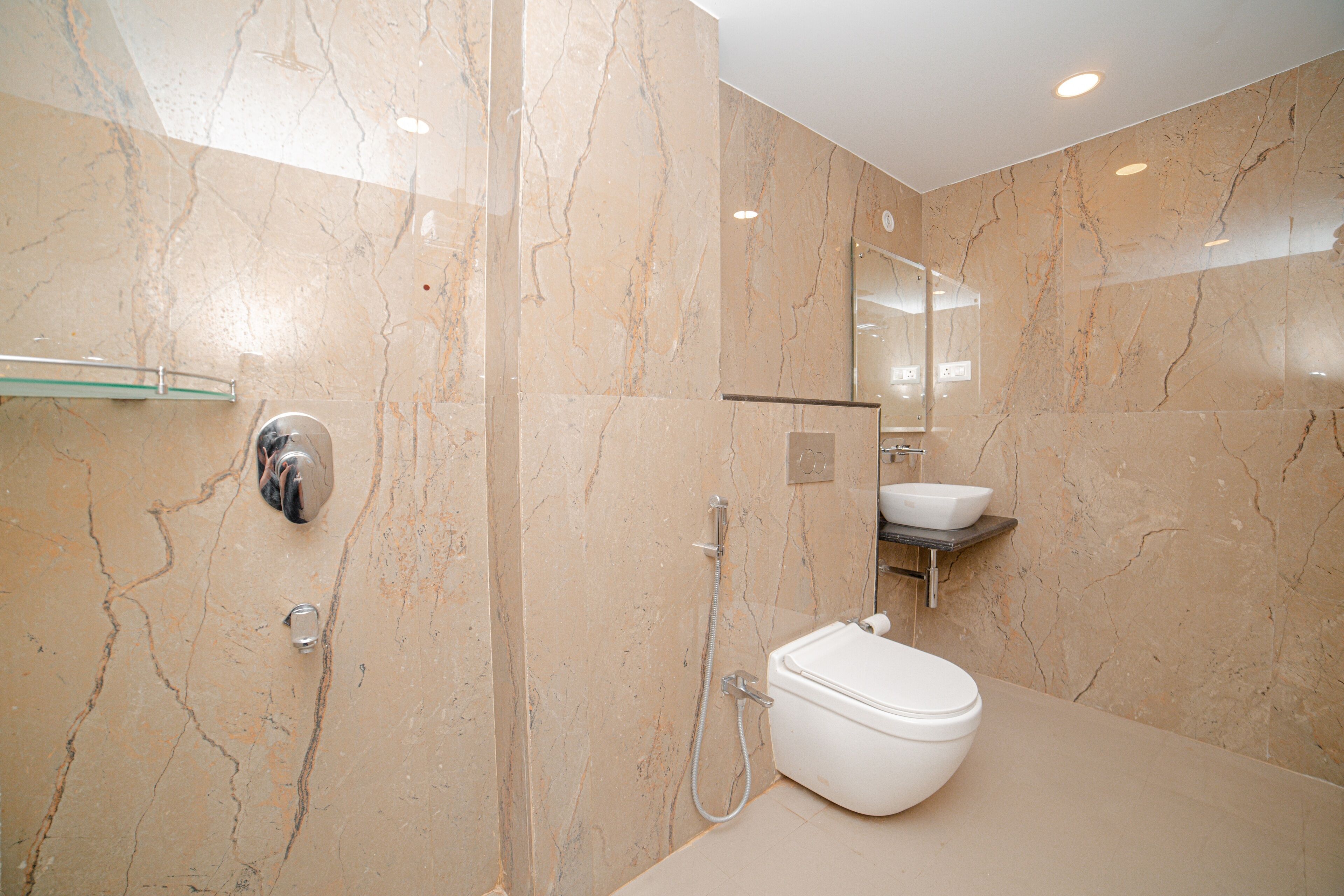 Un baño moderno con piso de mármol, cabina de ducha de vidrio, inodoro y lavamanos con espejo.