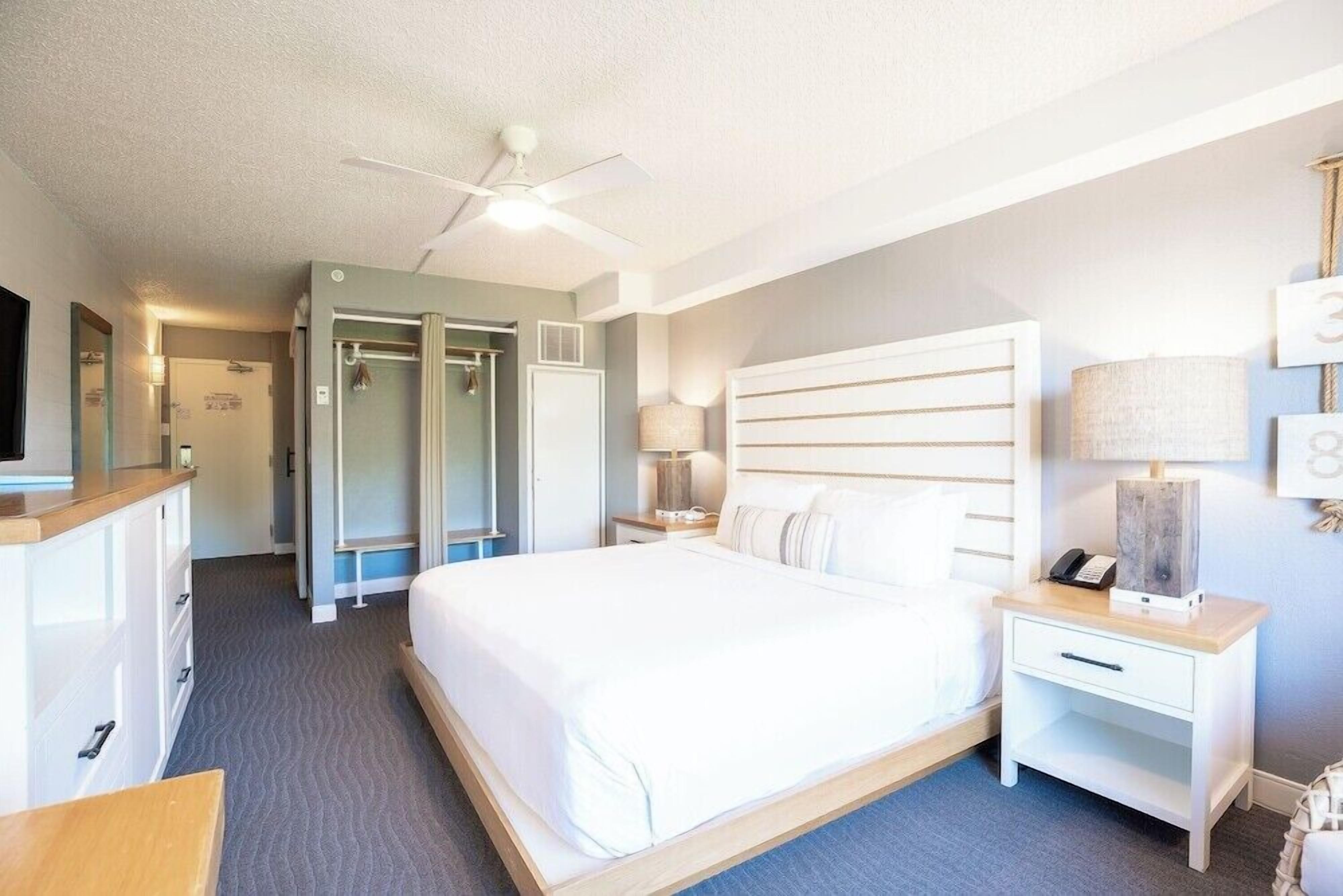 A hotel room with a bed, bedside tables, a ceiling fan, and a wardrobe.