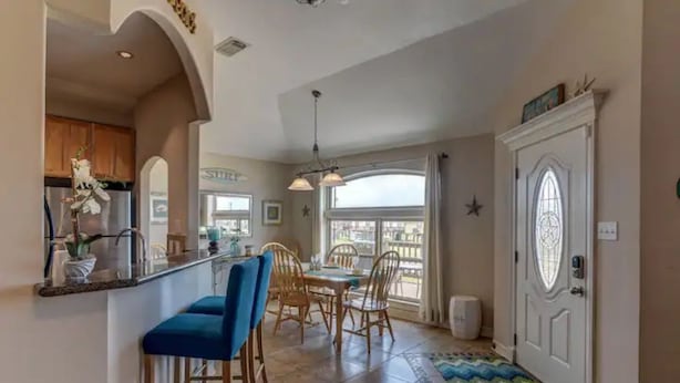 Una cocina con barra, sillas de madera, una mesa de comedor y un ventanal grande.