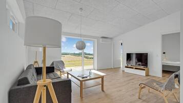 En moderne stue med et stort vindue, et fladskærms-tv og et hyggeligt opholdsområde.