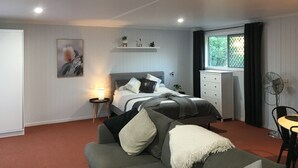 Et soveværelse med seng, sofa, et lille bord, et vindue med gardiner og en ventilator.