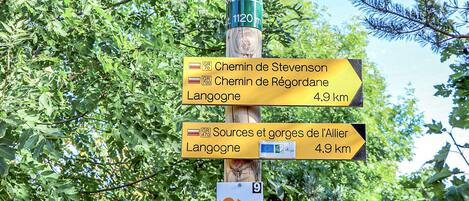 Un cartel con indicaciones y varias flechas que señalan diferentes destinos, incluyendo 'Chemin de Stevenson' y 'Chemin de Régordane', ambos que conducen a Langogne.