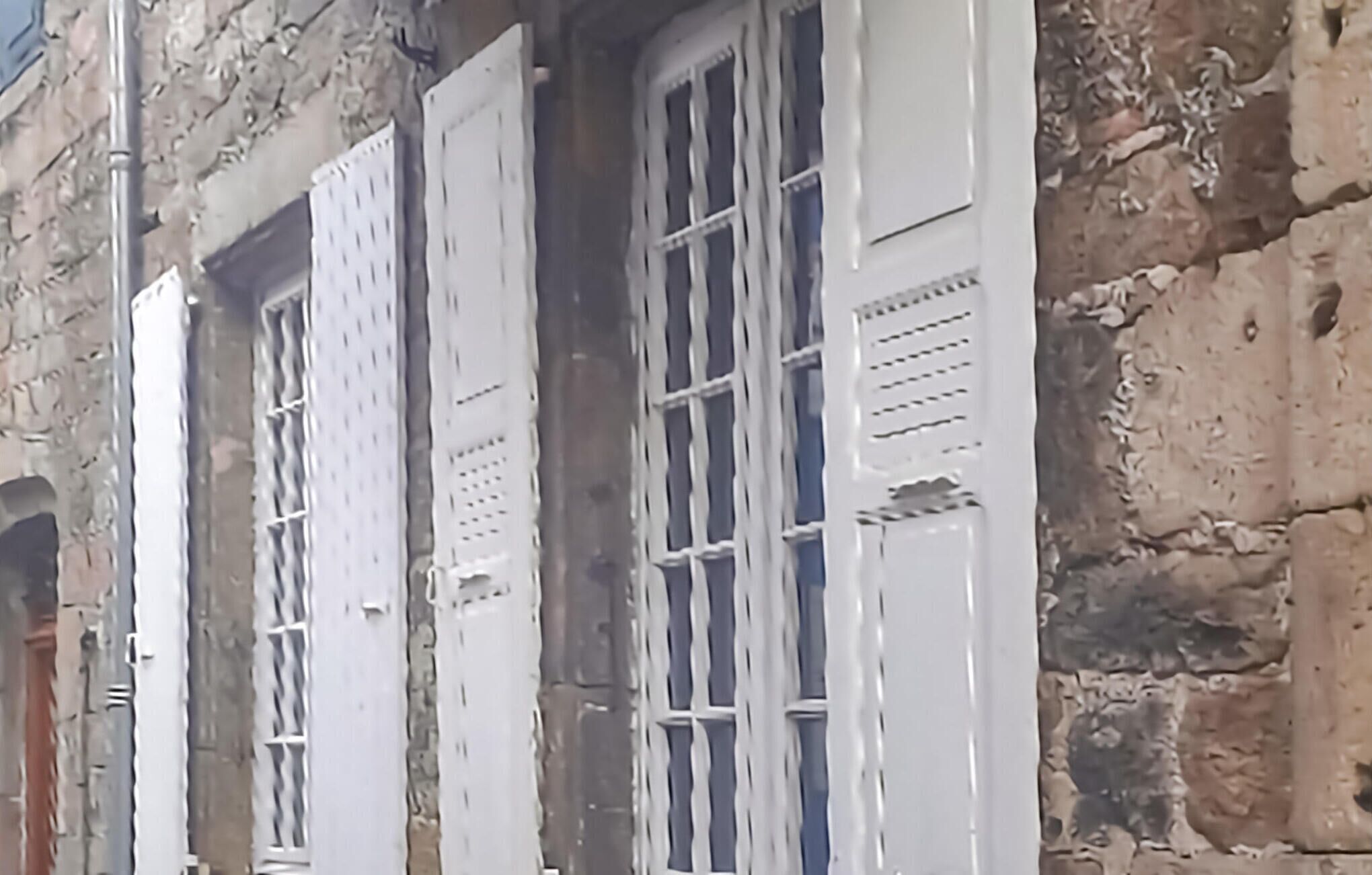 Une façade d’immeuble avec des volets blancs et des murs en pierre.