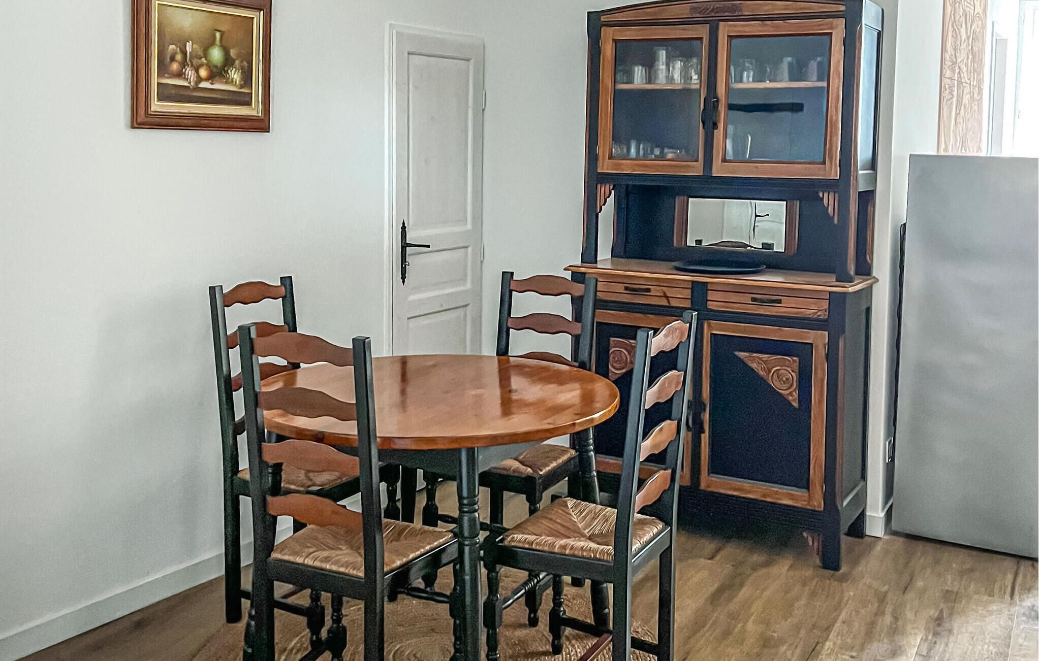 A dining area with a round wooden table and six chairs, a wooden cabinet with glass doors, and a white door.