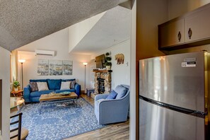 A modern living room with a blue sofa, a coffee table, and a patterned rug. There is a stone fireplace and a television mounted on the wall.