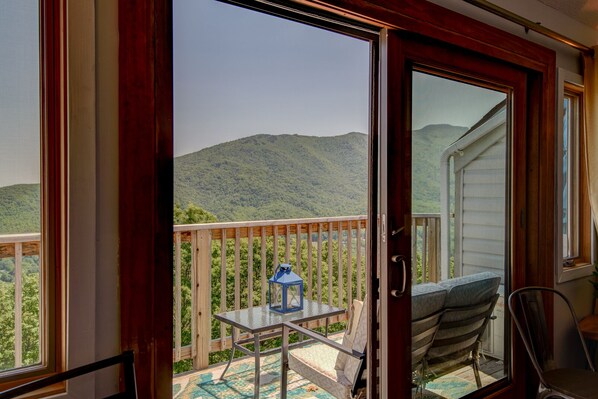 A balcony with a table and chairs, a lantern, and a view of a mountainous landscape.