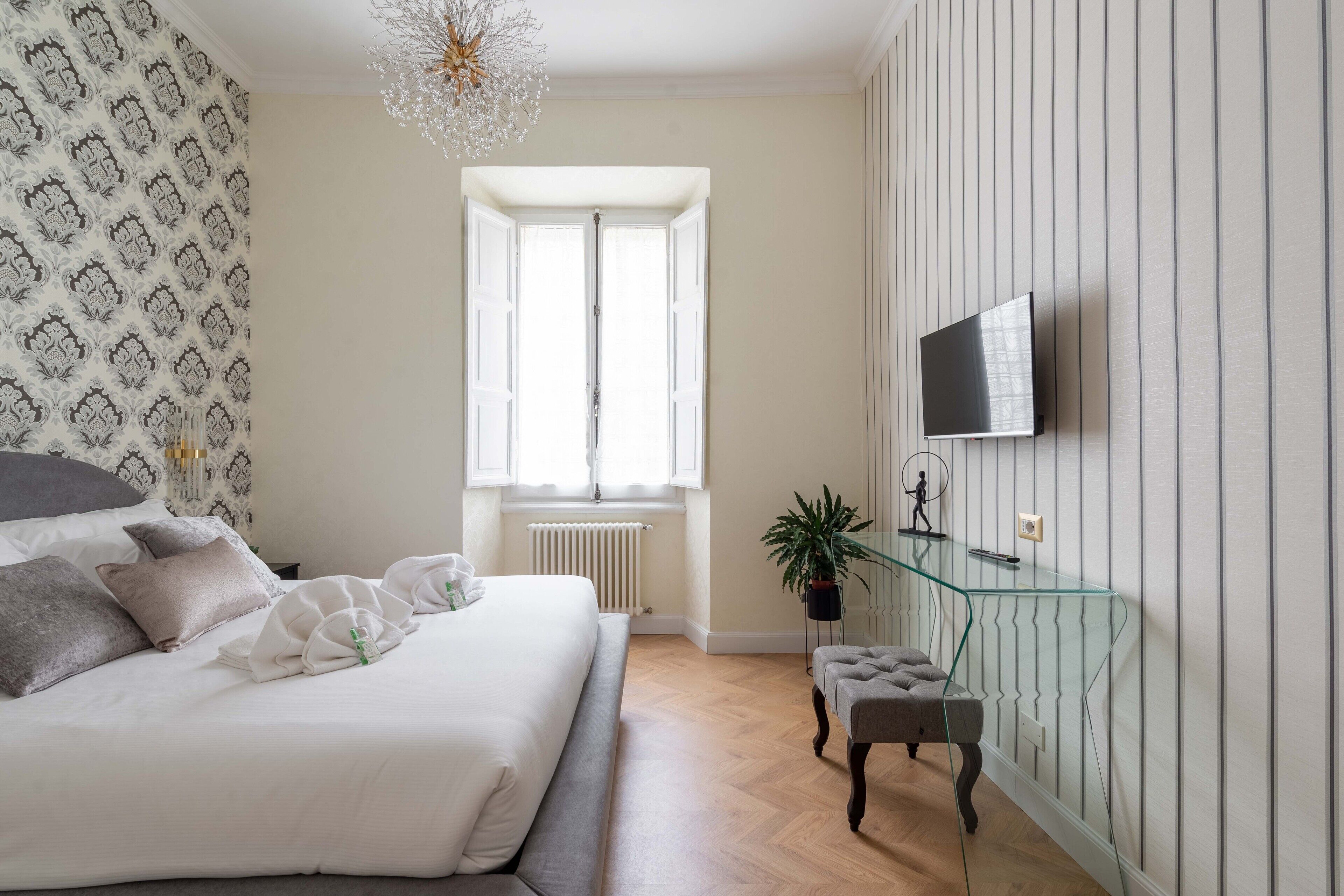 A bedroom with a bed, a glass TV stand, a radiator, and a window.
