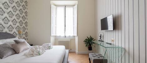 A bedroom with a bed, a glass TV stand, a radiator, and a window.