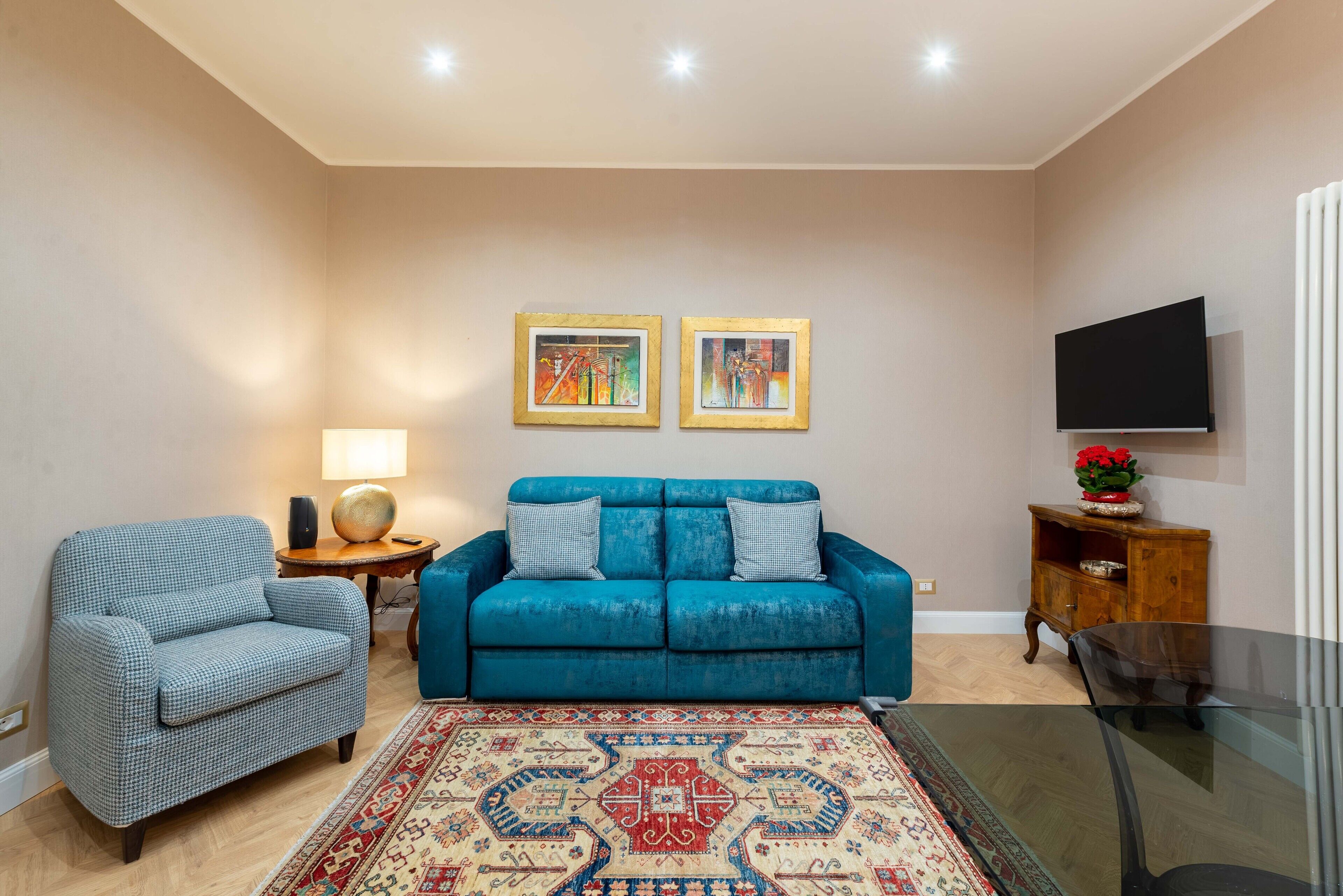 Ein Wohnzimmer mit einem blauen Sofa, einem gemusterten Sessel, einem Teppich und zwei gerahmten Kunstwerken an der Wand.