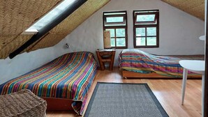 A small, cozy attic room with two beds, a small table, and a chair.