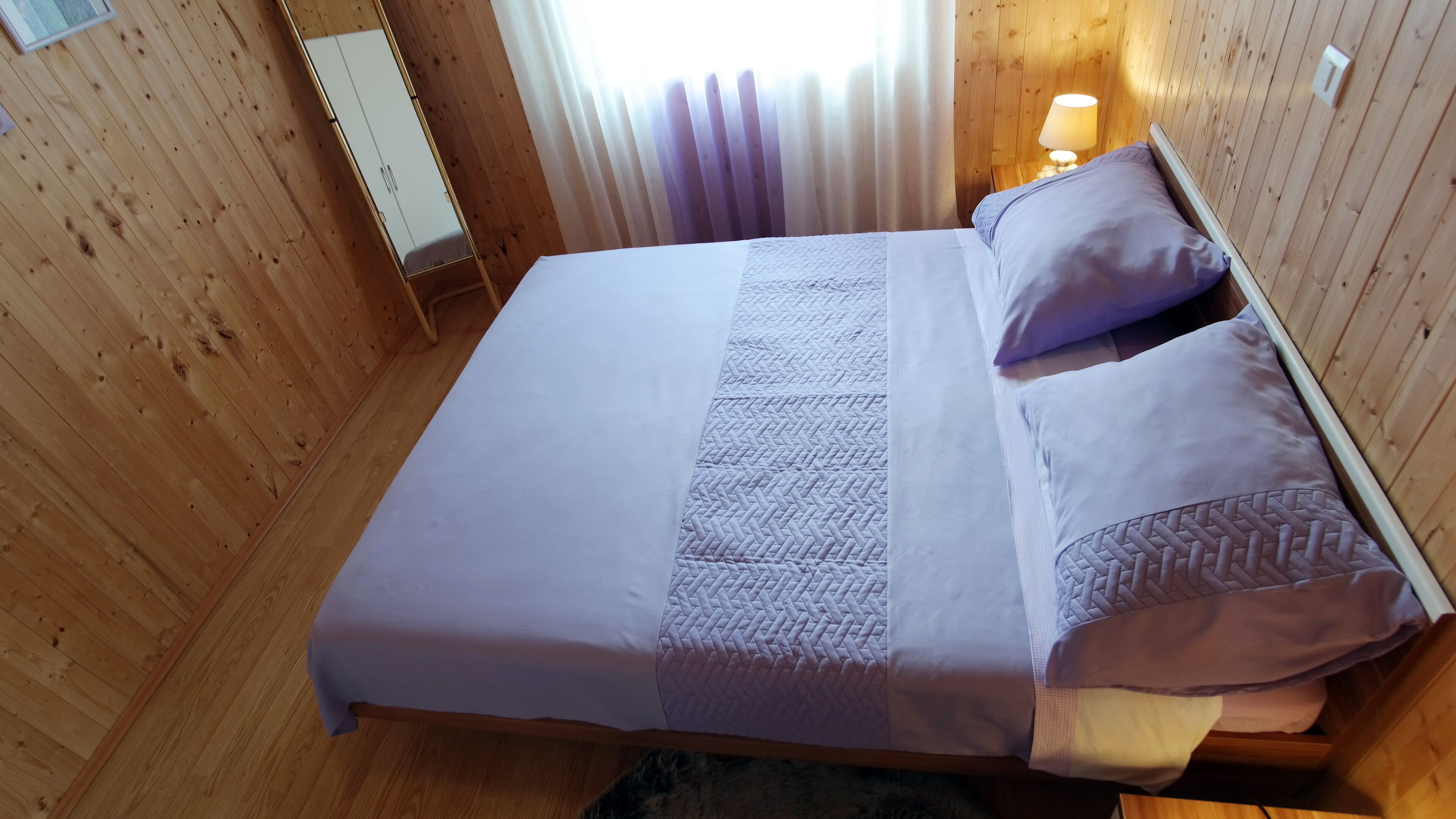 A wooden-paneled room with a bed, a nightstand, and a mirror.
