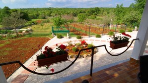 A balcony with a view of a landscaped garden, a stone bench, and a pathway leading to a green gate. - Vacation home near Rovinj quiet location with large garden, terrace, WLAN (Mrgani)
