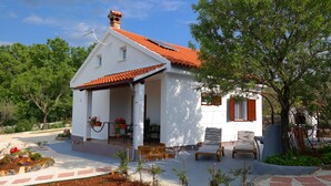 A small white house with a red-tiled roof, a covered porch with two chairs, and a garden with various plants and flowers. - Vacation home near Rovinj quiet location with large garden, terrace, WLAN (Mrgani)