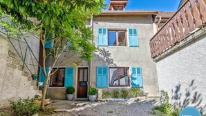 A two-story building with a gravel driveway, potted plants, and a visible manhole cover. - La Cachette du Lac – Near the Lake (MENTHON-SAINT-BERNARD)