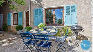 A patio with a table set for four, blue shutters, a grill, and a view of the surrounding area. - La Cachette du Lac – Near the Lake (MENTHON-SAINT-BERNARD)