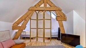 A loft bedroom with a sloped ceiling, a bed, a TV, and a window. - La Cachette du Lac – Near the Lake (MENTHON-SAINT-BERNARD)