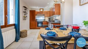 A modern kitchen with wooden cabinets, a dining table set for six, and pendant lighting. - La Cachette du Lac – Near the Lake (MENTHON-SAINT-BERNARD)