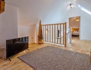A modern loft bedroom with a sloped ceiling, a large window, a TV, a wooden gate, and a cozy seating area. - La Cachette du Lac – Near the Lake (MENTHON-SAINT-BERNARD)