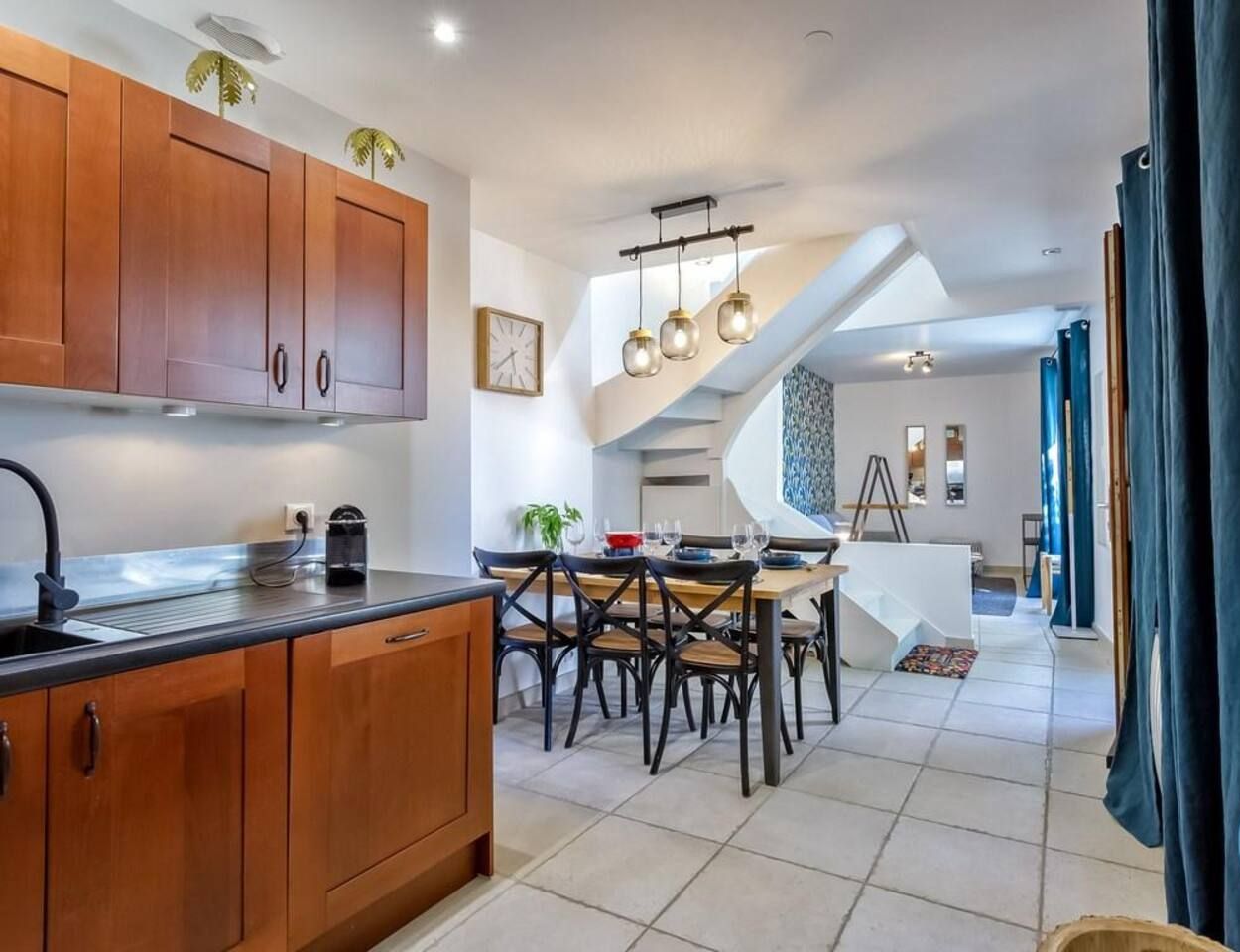 Une cuisine moderne avec des meubles en bois, un coin repas avec une table et des chaises blanches, et un escalier menant à un autre niveau.