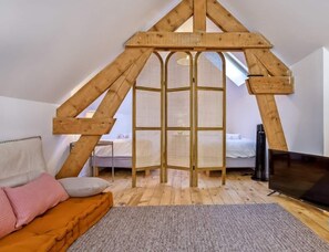 Un dormitorio tipo loft con techo inclinado, una cama, un televisor y un ventanal.