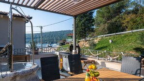 Un espacio de estar al aire libre con vista a un lago y barcas, que incluye una mesa con fruta y una parrilla.
