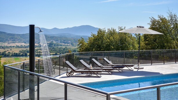 Una piscina en la azotea con una cascada, sillones de descanso y vistas a montañas distantes.