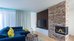 Una sala de estar moderna con chimenea de piedra, un sofá azul y un televisor de pantalla plana montado en la pared.
