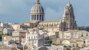 Un bâtiment historique doté d’un dôme et d’un clocher imposants, entouré d’autres bâtiments de style méditerranéen traditionnel.