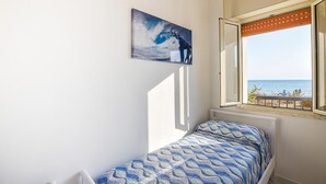 Une chambre avec un lit, une fenêtre donnant sur la mer et un tableau représentant une vague accroché au mur.