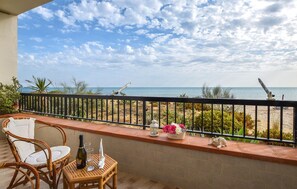 A balcony with wicker chairs, a small table with a bottle and glasses, a flower vase, and a view of the beach and ocean. - 2 bedroom nice home in Santa Croce Camerina (Santa Croce Camerina)