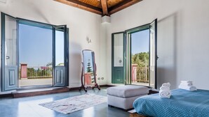 A bedroom with a large bed, a bench, and a mirror. There are two open doors leading to a balcony. - Charming Sea View Villa close to beach (Syracuse)