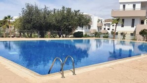 Ein Schwimmbecken mit einer Metallleiter, umgeben von einer gefliesten Terrasse und Bäumen.