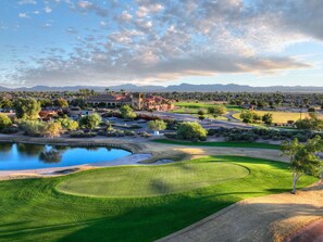 Un parcours de golf avec un étang, des bâtiments et des montagnes en arrière-plan.