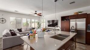 Cozinha moderna com ilha central, eletrodomésticos de aço inoxidável e área de refeições com sofá e mesa de centro.
