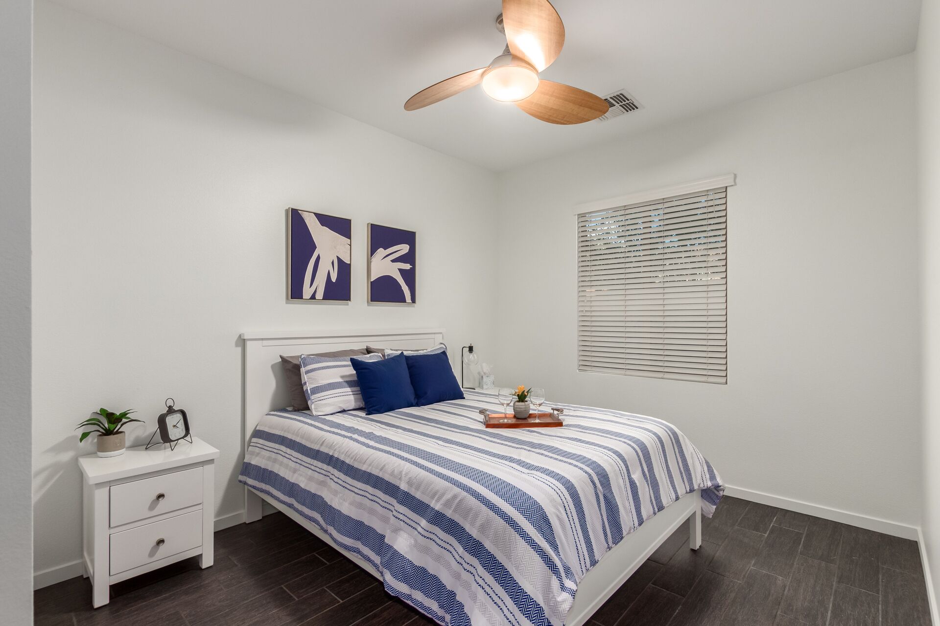 A bedroom with a bed, a nightstand, a ceiling fan, and artwork on the wall.