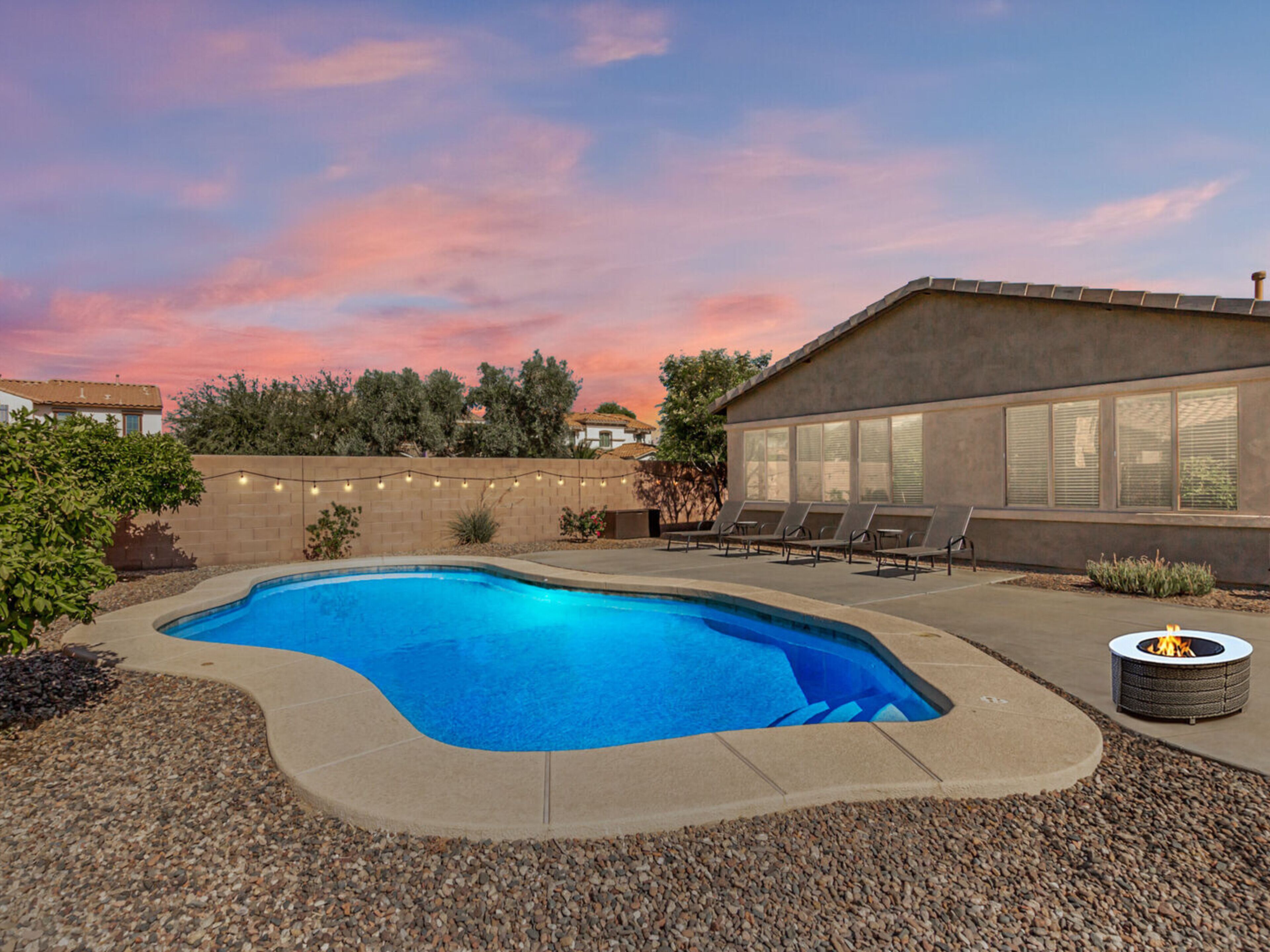 A swimming pool with a fire pit, surrounded by a patio area with lounge chairs.