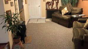 Ein Wohnzimmer mit braunem Sofa, einem kleinen Tisch, einer Zimmerpflanze und einer Tür.