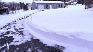 Eine verschneite Straße führt zu einer Wohngegend mit einem großen Haus und einer Garage.