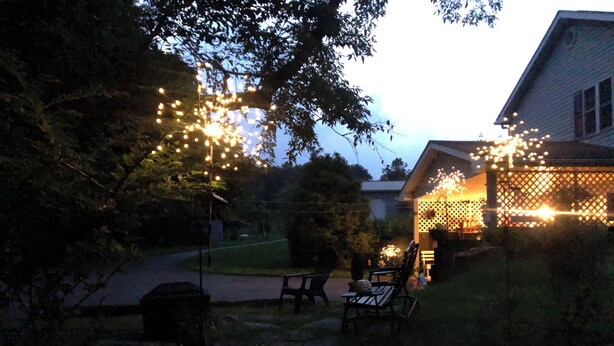 Ein Haus mit Veranda, geschmückt mit Lichterketten, Rasen und Gartenmöbeln.