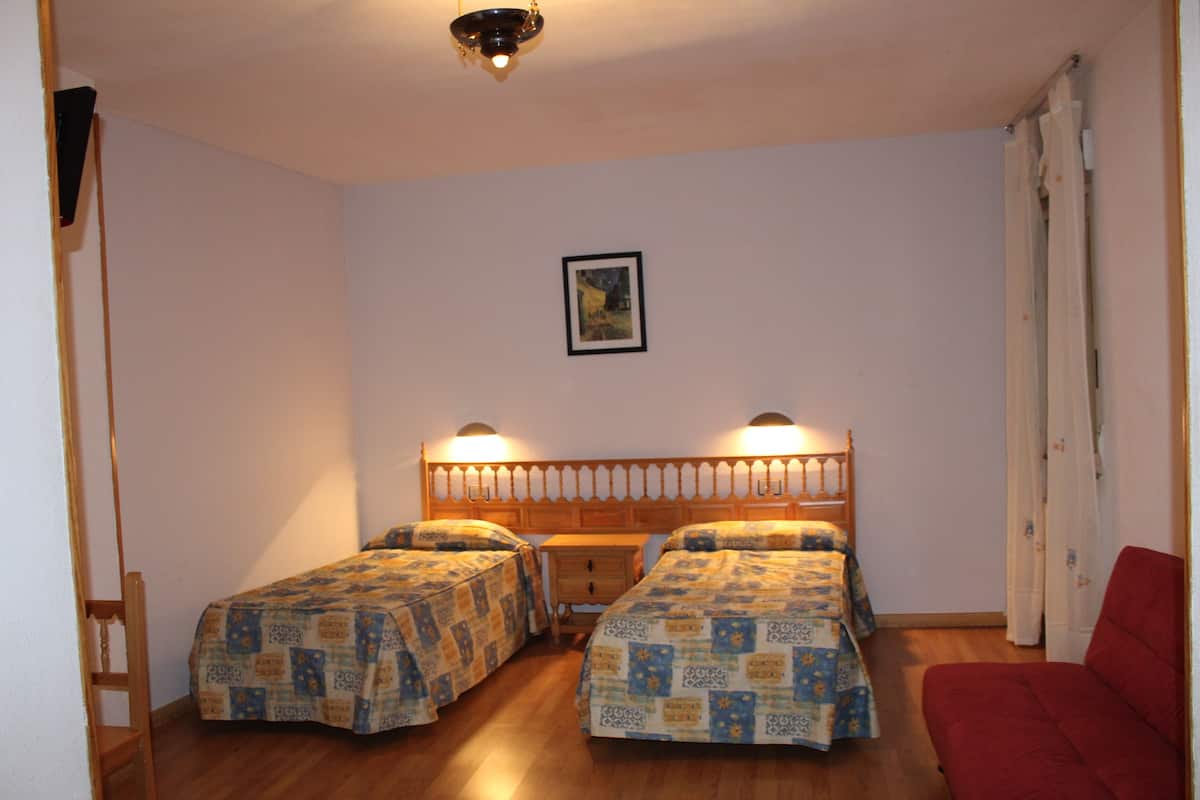 A room with two single beds, a wooden headboard, a small table, and a red chair.