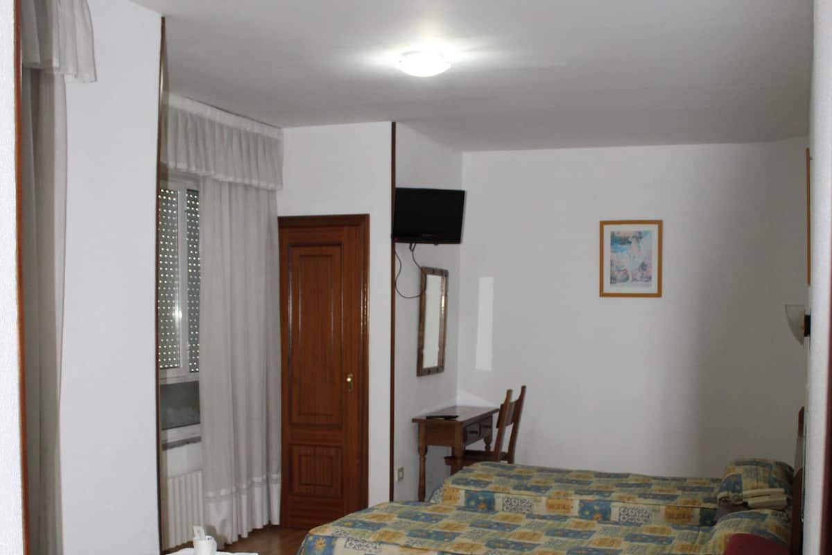A room with two beds, a red chair, a wooden desk, and a television.