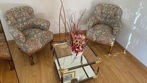 A room with two patterned armchairs, a glass-top coffee table with a floral centerpiece, and a lamp. - Hotel Santa Clara (Monforte de Lemos)