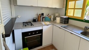 Et lille køkken med hvide skabe, en gaskomfur, en ovn, en vask og et vindue med skodder.