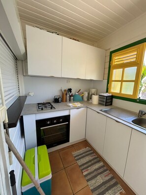 Eine kleine Küche mit weißen Schränken, einem Gasherd, einem Backofen, einer Spüle und einem Fenster mit Jalousien.