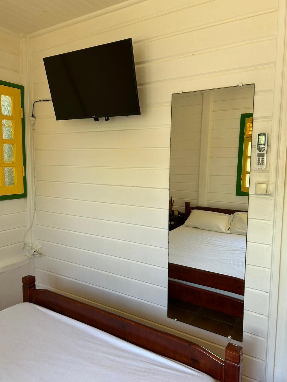 Una stanza con un letto, una televisione a muro e uno specchio che riflette un letto e un telefono.